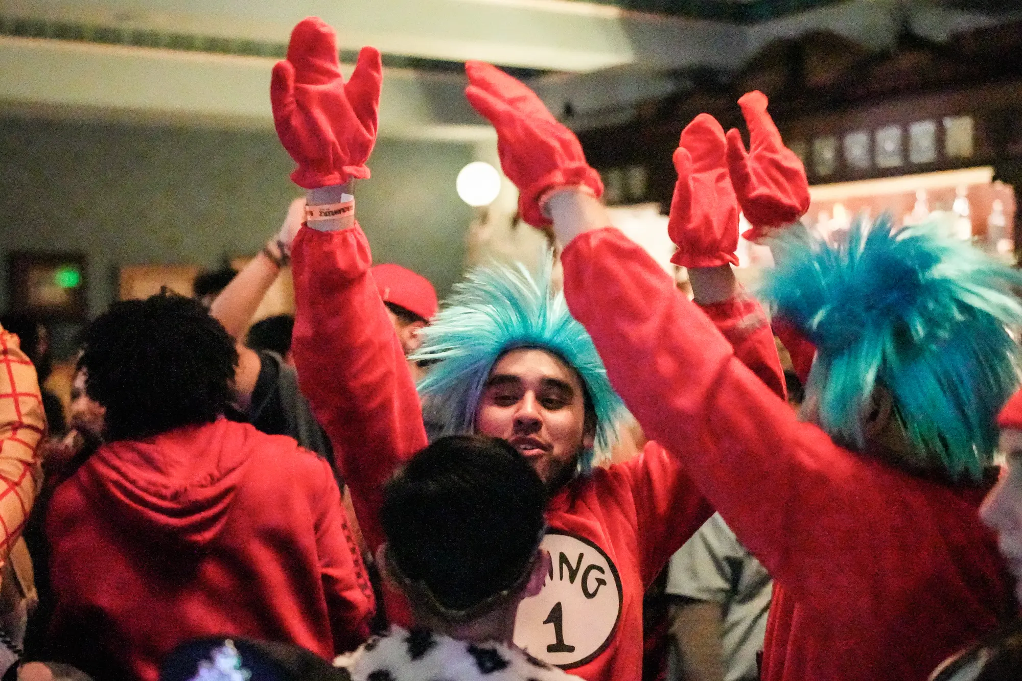 Guests in a Thing 1 costume with a blue wig and red gloves cheer with their hands in the air on the dance floor.