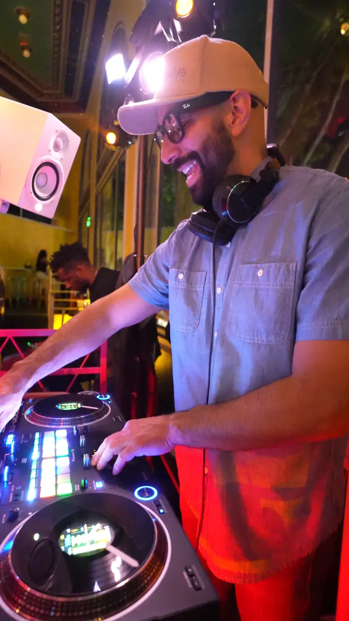 DJ Mojo laughing as he mixes under colored lights at The Long Weekend in San Francisco