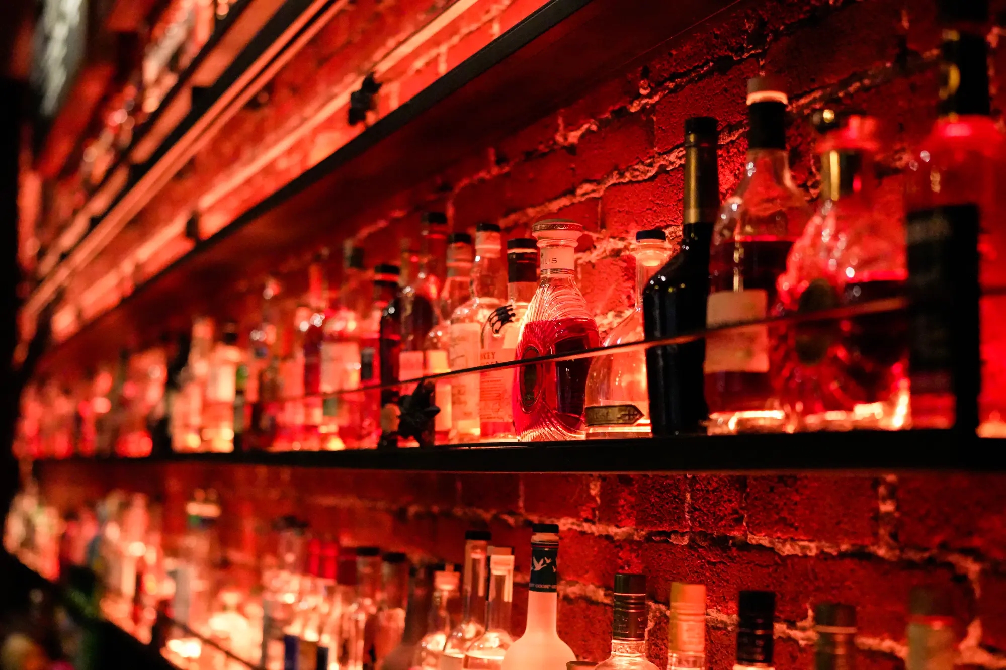 Shelves of liquor bottles glowing in red and orange light behind a bar.